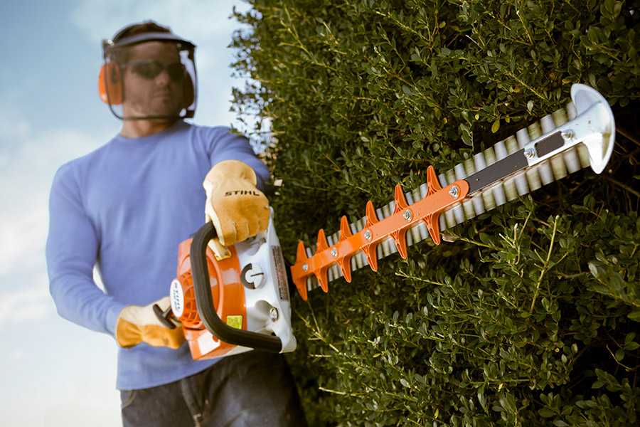 Man using STIHL hedge trimmers to trim a large hedge