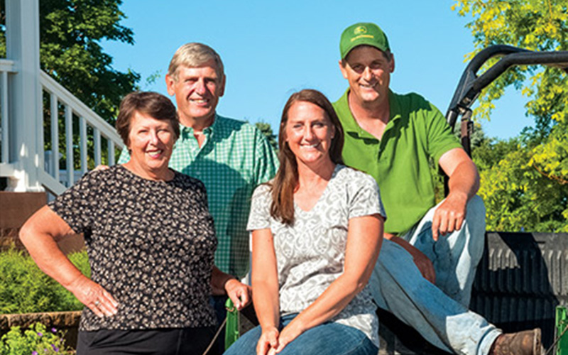 Family standing in front of their house beside a John Deere Gator