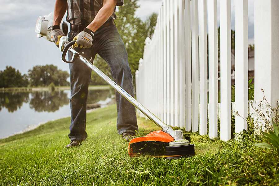 Man using a STIHL trimmer to cut grass around a fence