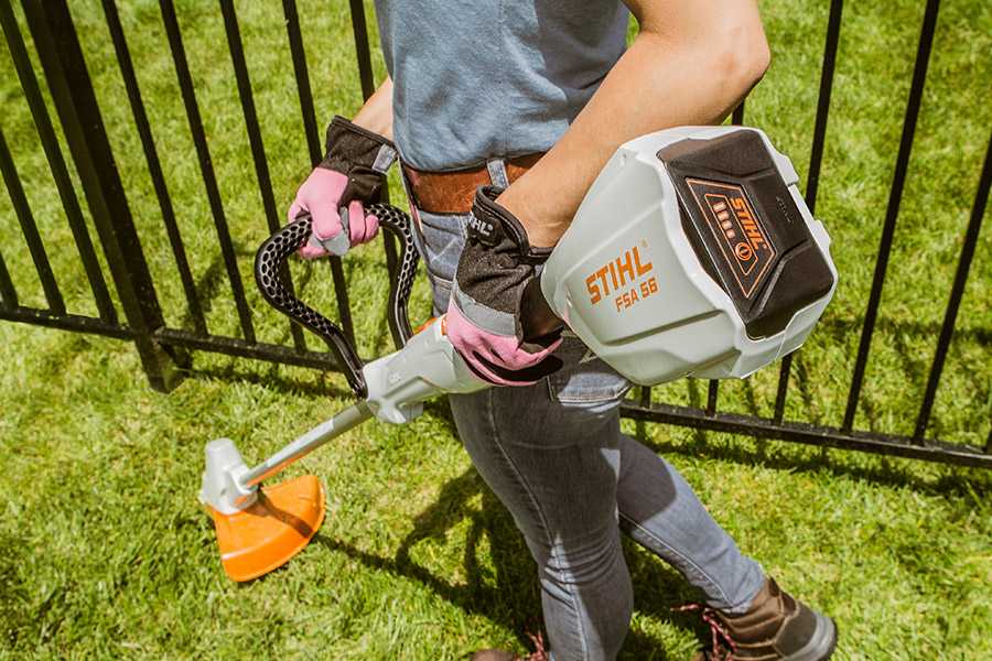 Woman using a STIHL FSA 56 battery trimmer to cut grass around a fence